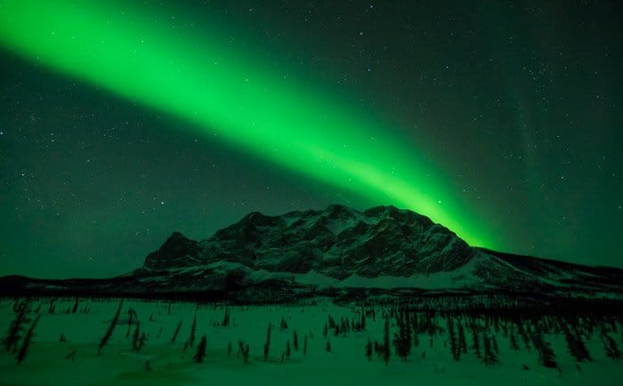 Foto de la aurora boreal sobre un paisaje montañoso.  Fotografía de invierno.