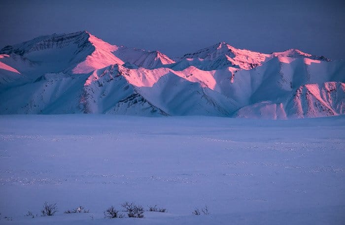 colinas cubiertas de nieve al atardecer con resplandor rosado en ellos