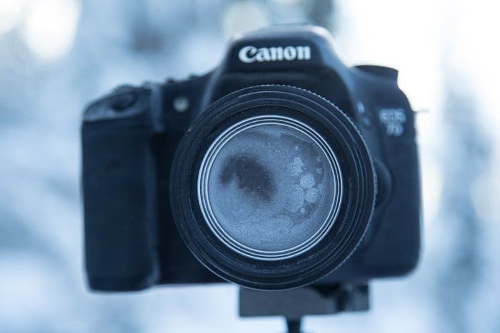 Cámara Canon sobre trípode con lente y cuerpo de la cámara completamente cubiertos de escarcha, fotografía de invierno.