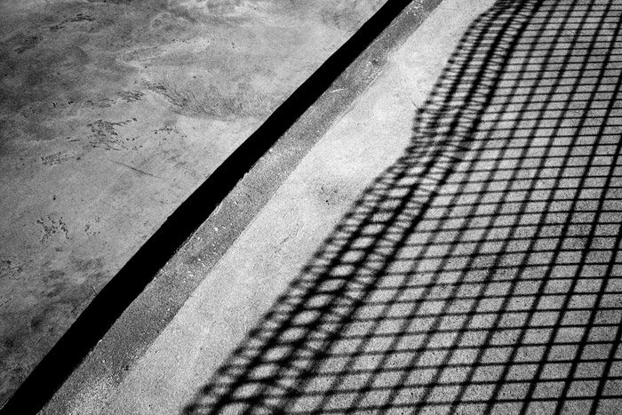 Una fotografía sombría en blanco y negro de hormigón con la sombra de una valla, que combina luz y sombra para la fotografía abstracta.