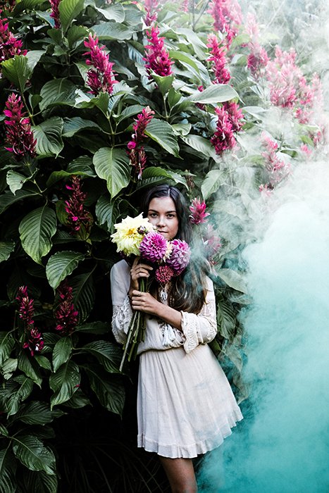 Una niña de pie y sosteniendo flores, una gran nube de humo viene hacia ella desde el lado derecho.