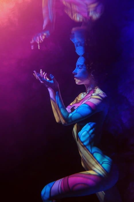 Sesión de fotos submarina artística de una modelo femenina rodeada de luz coloreada posando bajo el agua