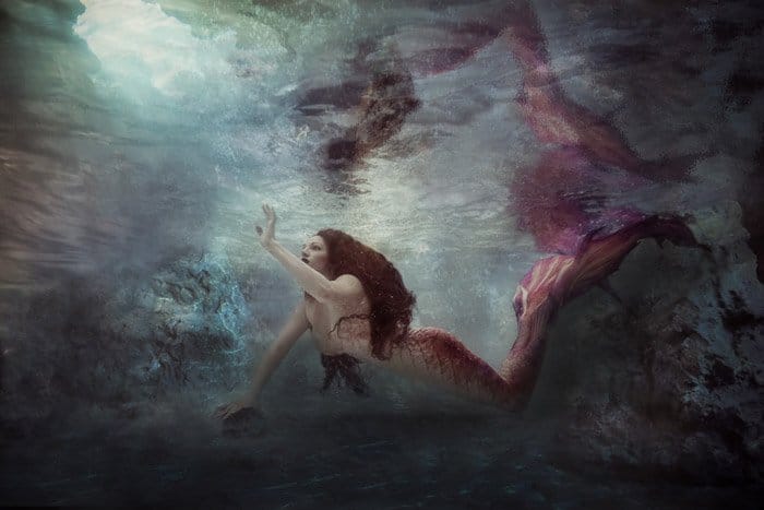 Un retrato submarino surrealista de un modelo femenino en cola de sirena posando bajo el agua