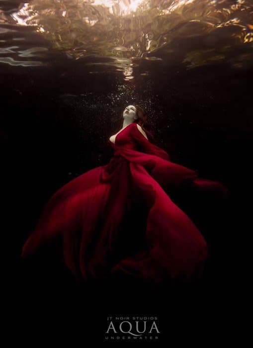 Sesión de fotos submarina atmosférica de una modelo femenina en un vestido rojo posando bajo el agua