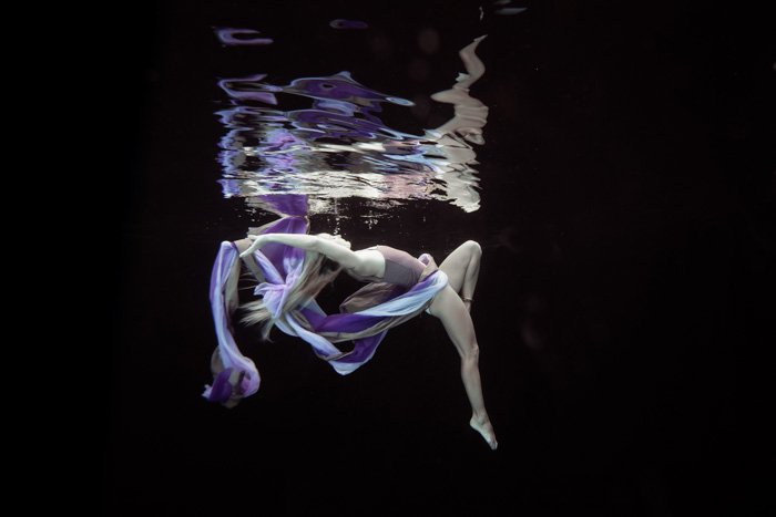 Impresionante toma de fotografía submarina de una niña posando con tela púrpura y mientras nadaba bajo el agua