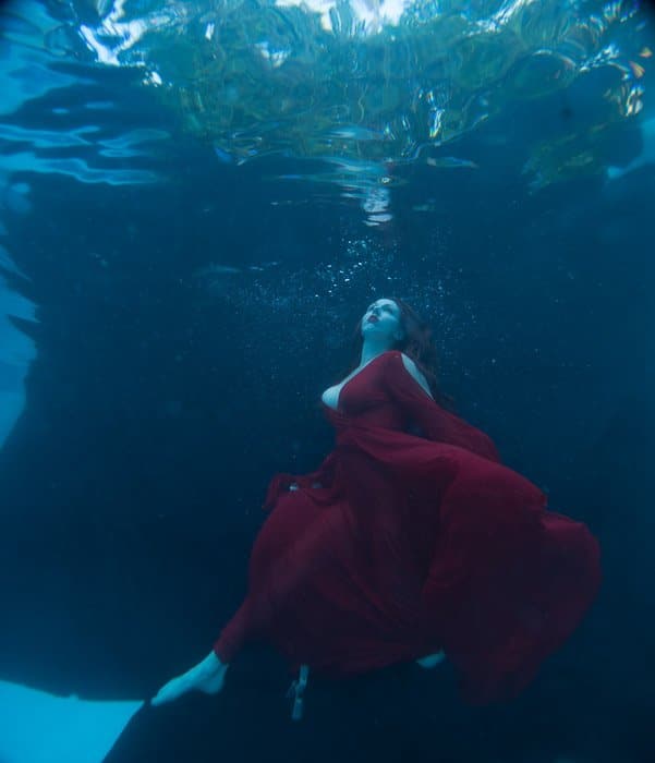 Una mujer hermosa en vestido rojo que fluye posando bajo el agua