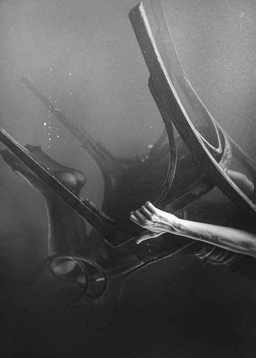 Fotografía subacuática artística monótona que muestra a una persona en una silla de madera cayendo aún más bajo el agua