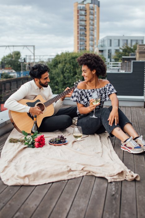 Imagen de una pareja romántica haciendo un picnic mientras el novio toca una guitarra