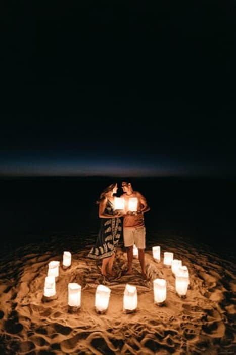 feliz pareja de pie en la playa, rodeado de linternas