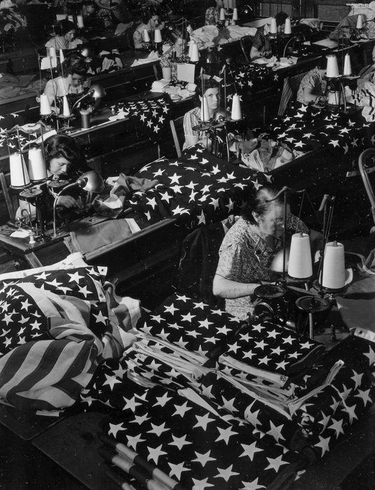 Fotografía en blanco y negro de mujeres cosiendo banderas estadounidenses por la fotógrafa de guerra Margaret Bourke-White