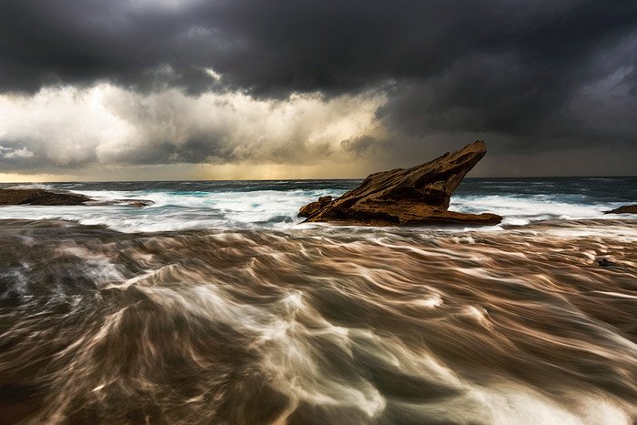 Afloramiento de la plataforma rocosa en las agitadas aguas del mar, cielos nublados oscuros, una puesta de sol dorada en el horizonte - ajustes de fotografía de agua