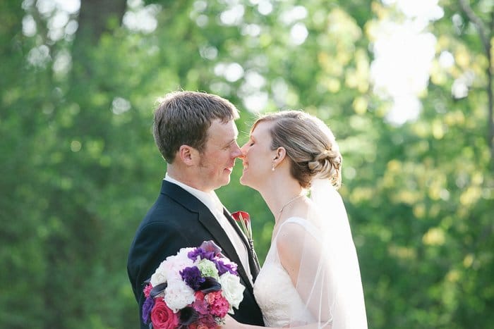 Una novia y un novio sonrientes al aire libre contra un fondo de hojas verdes a punto de besarse: los mejores consejos para editar fotos de bodas