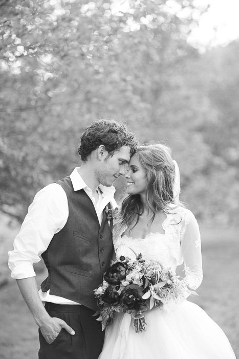 foto en blanco y negro de recién casados ​​parados afuera, mirándose a los ojos, tocándose las frentes