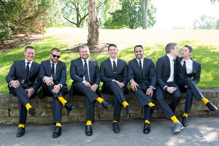 Foto de boda humorística de siete padrinos de boda sentados en una pared, todos vistiendo calcetines amarillos