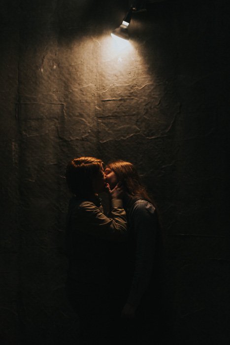 Una pareja besándose frente a una pared texturizada con una sola fuente de luz