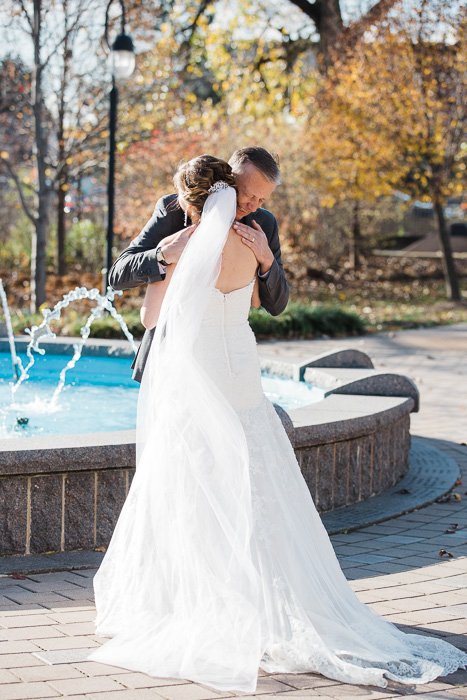 Momento dulce del día de la boda de una novia abrazando a su padre frente a una fuente
