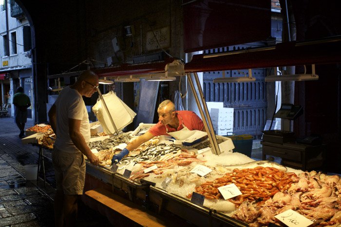 Un hombre interactuando con un vendedor del mercado en un mercado de pescado en Venecia - fotos de Italia