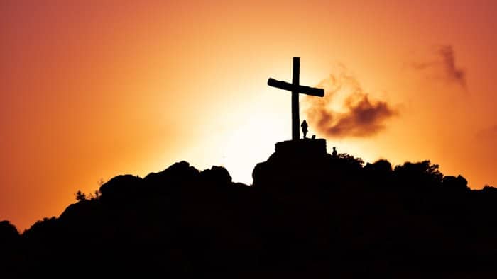 Fresca fotografía de la silueta de una niña junto a una cruz gigante en una montaña al atardecer