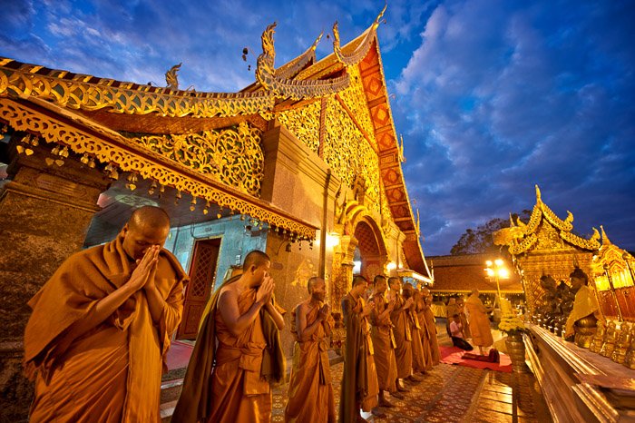 Una línea de monjes budistas rezando fuera de un templo al anochecer: profundidad de campo superficial vs profunda
