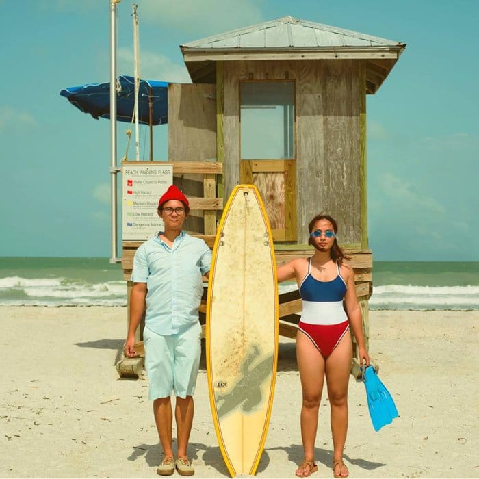 pareja en la playa posando para una foto sosteniendo una tabla de surf entre ellos - estilos de fotografía de teléfonos inteligentes