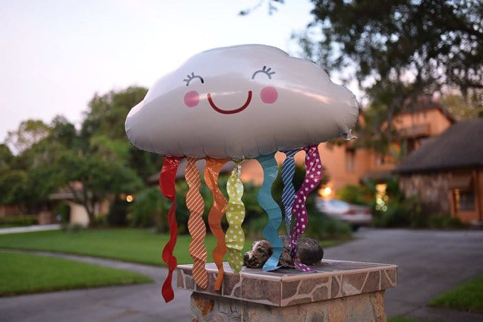 un globo con forma de nube con serpentinas de colores y una sonrisa, flotando en un barrio residencial