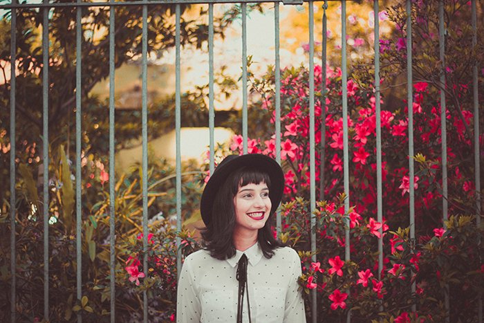 Una modelo femenina de pie al aire libre frente a las flores y sonriendo naturalmente: cómo sonreír en imágenes
