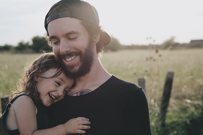Dulce retrato de un padre sonriente y una hija joven al aire libre: cómo sonreír para las fotografías