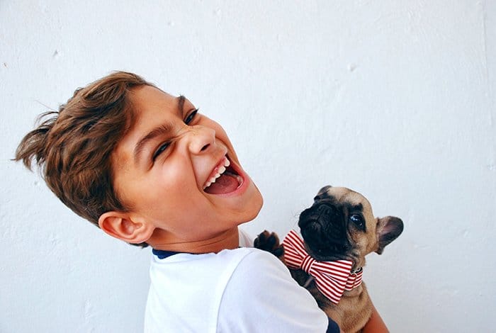 Divertido retrato de un joven riendo sosteniendo un perro pequeño - gente sonriente