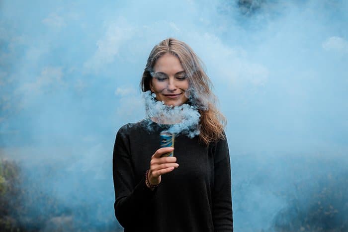 Un retrato creativo de una mujer sosteniendo una granada de humo azul claro cerca de su cara