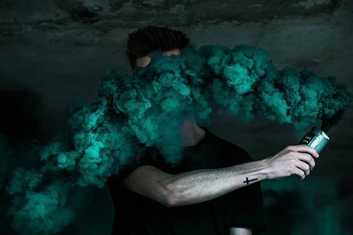 Un retrato creativo de la fotografía de la bomba de humo de un hombre que sostiene una granada de humo verde cerca de su cara