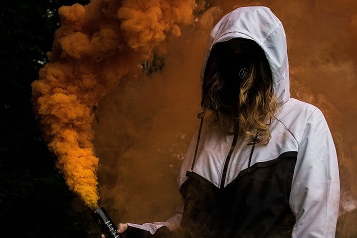 Retrato sin rostro de una mujer sosteniendo granadas de humo naranja
