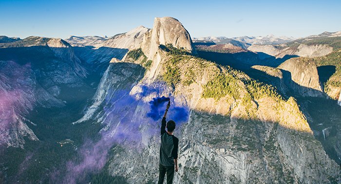Impresionante retrato de un hombre agitando granadas de humo azul en un paisaje montañoso