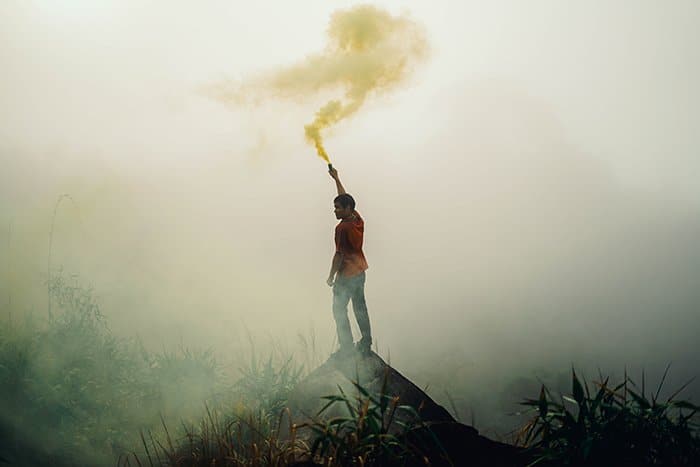 Retrato atmosférico de un hombre agitando granadas de humo en un entorno paisajístico