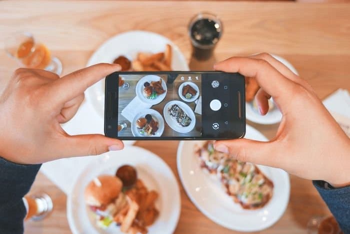foto de manos sosteniendo un teléfono inteligente para tomar una foto de platos de comida