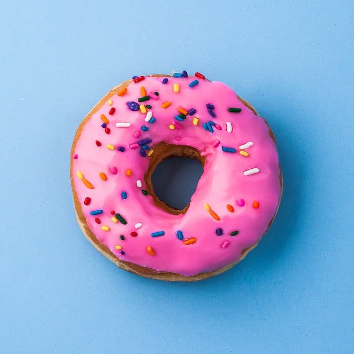 Una fotografía cenital de un donut helado rosa sobre fondo azul claro