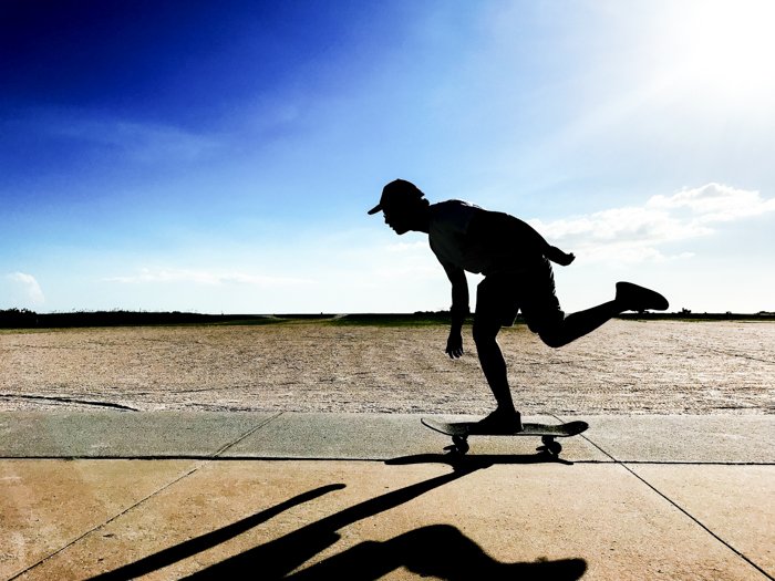 Foto de un hombre de skate en movimiento con fondo de cielo azul