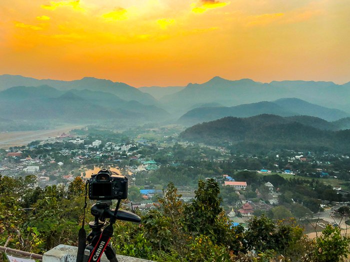 Una cámara en un trípode dirigida hacia un paisaje impresionante con cielo amarillo: cómo ganar dinero con la fotografía
