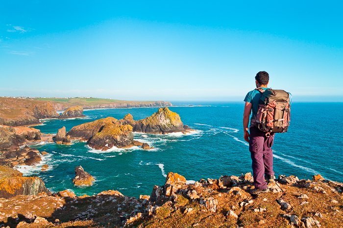 Un mochilero macho de pie sobre acantilados rocosos con vistas a un fantástico paisaje marino