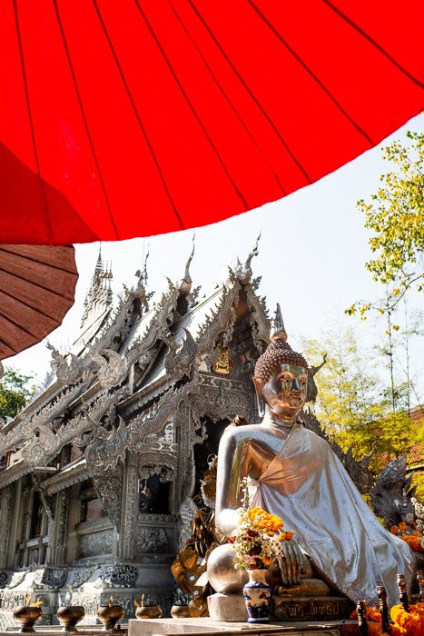   Una estatua de buda bajo una sombrilla roja frente a un templo: cómo eliminar el resplandor en las fotos