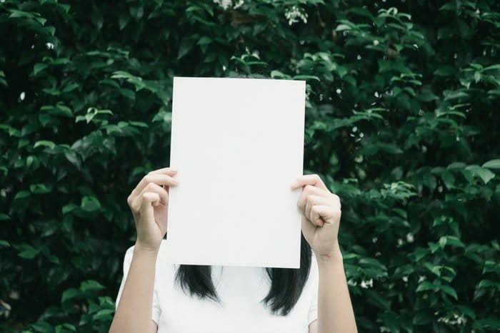 Una mujer sosteniendo una hoja de papel en blanco sobre su rostro