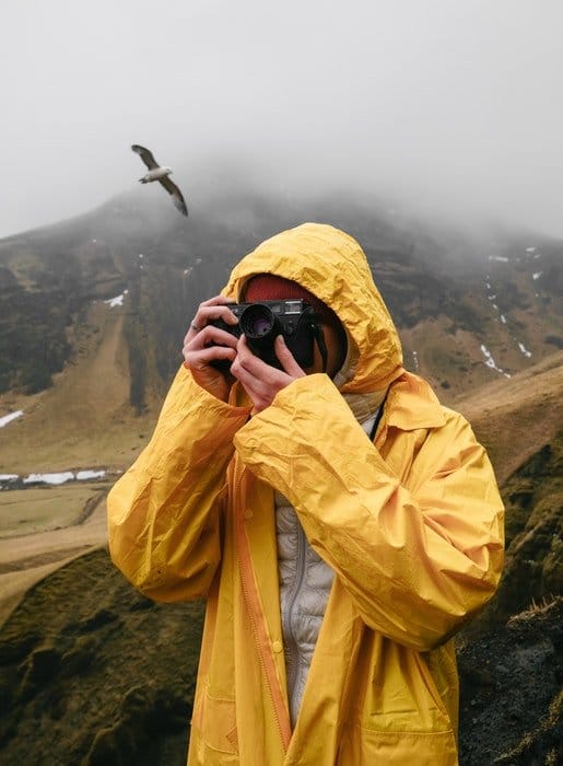 un fotógrafo en amarillo disparando en un día lluvioso en las montañas con un pájaro detrás de él