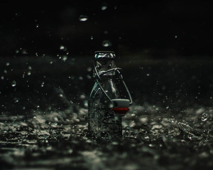 Fotografía de producto atmosférico de botella de vidrio salpicada con lluvia que cae