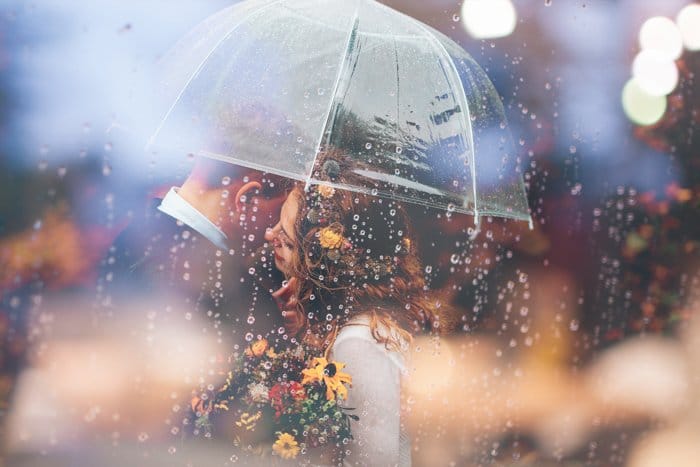 Fotografía de boda de ensueño de una pareja abrazándose bajo un paraguas