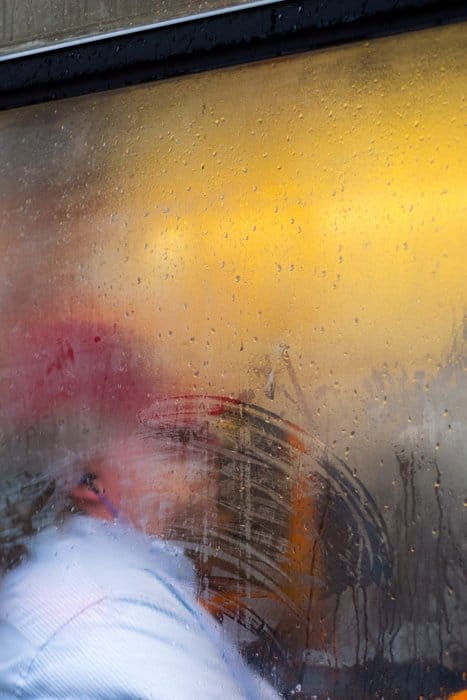 Un retrato de una persona disparada a través de una ventana salpicada de lluvia