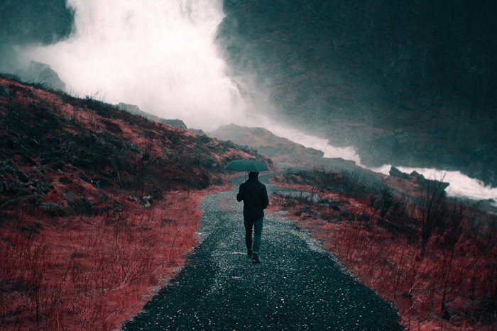 Imagen de lluvia oscura y temperamental de una persona caminando por un paisaje con un paraguas