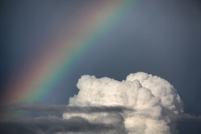 Una impresionante imagen de arco iris junto a una nube blanca y esponjosa.