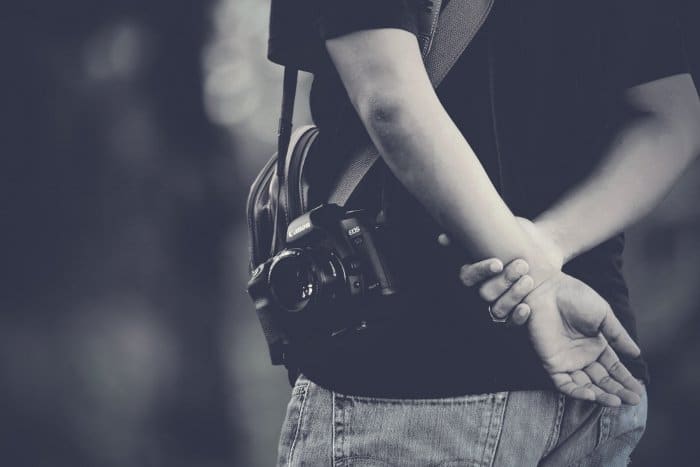 Un primer plano en blanco y negro de un hombre con una cámara discreta con lente de 50 mm para tomar fotos callejeras sinceras