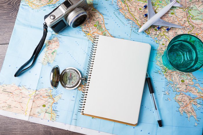 Una fotografía cenital de una cámara, un cuaderno, un bolígrafo y un modelo de avión en la parte superior de un mapa del mundo.