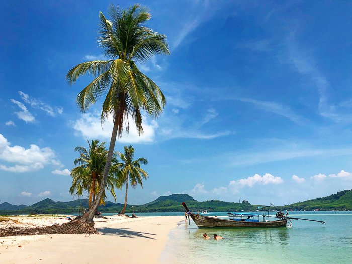 Una escena de playa tropical de ensueño con palmeras y bote de madera.