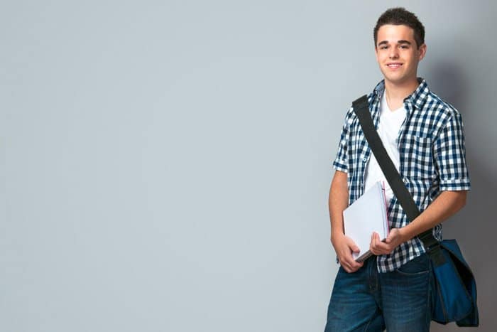 Un retrato escolar de un adolescente sonriente con una mochila de pie sobre el fondo de la pared: consejos para retratos escolares de calidad